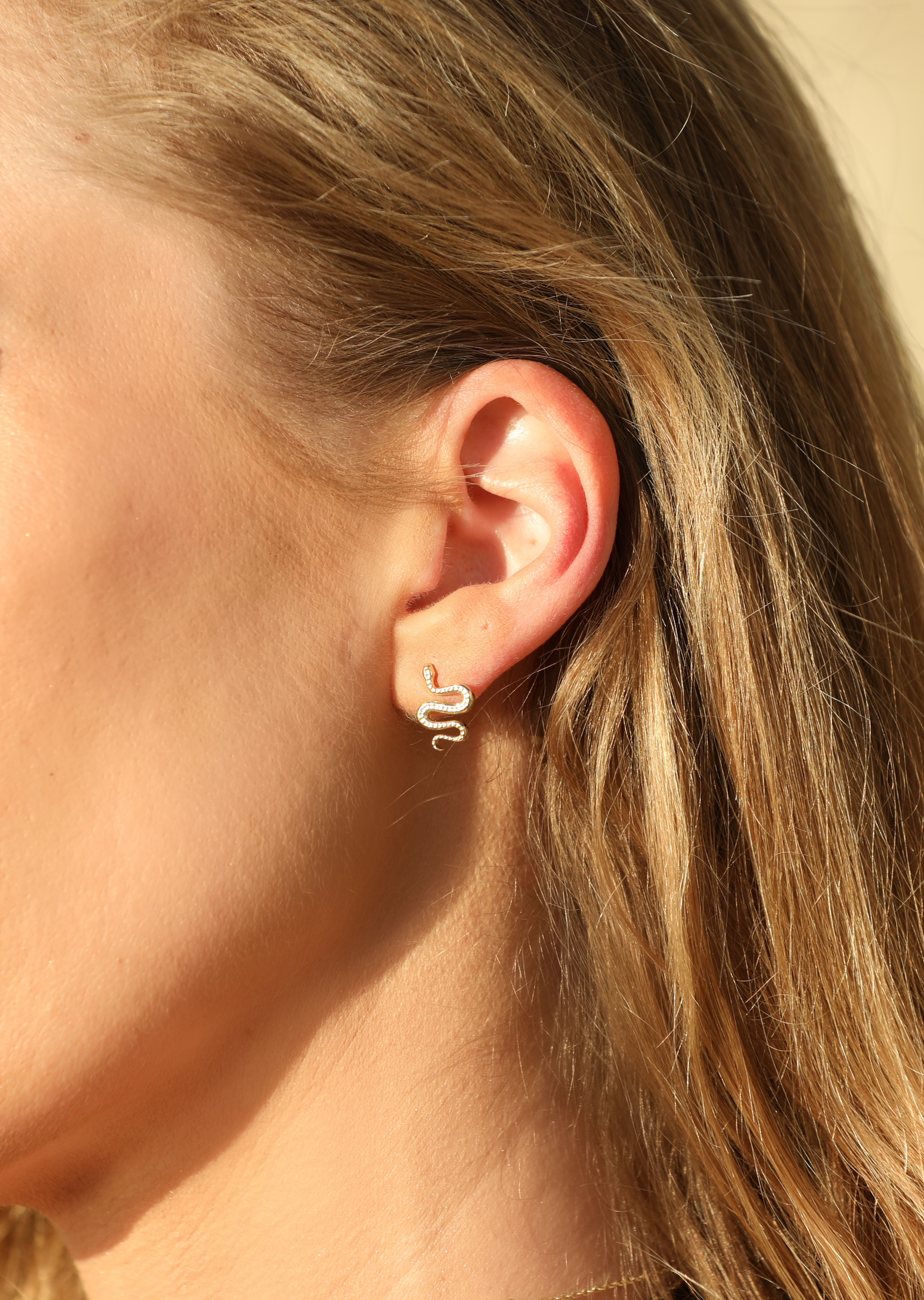 Ular serpent earrings worn on bare skin, front view